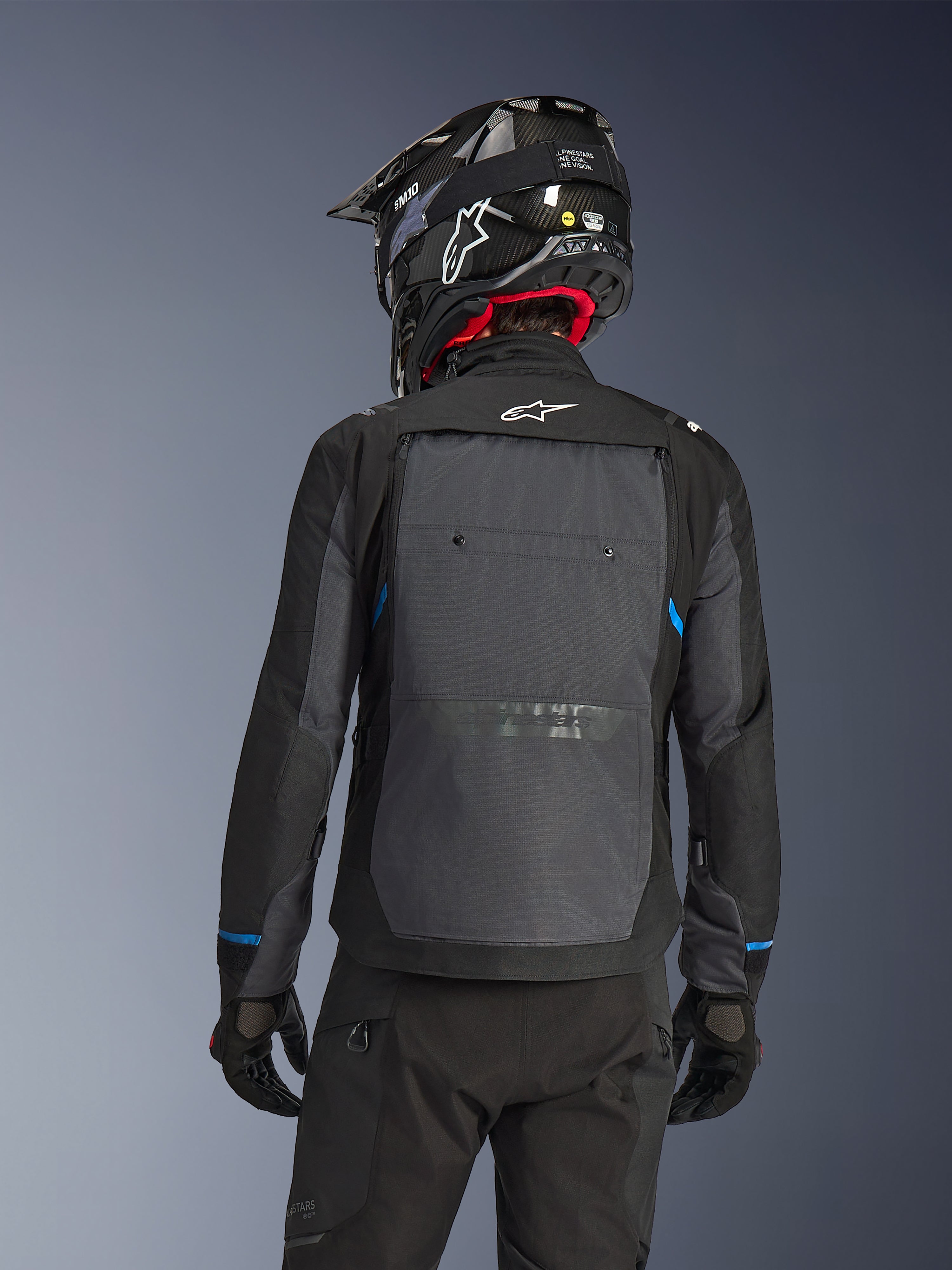 Piloto visto de costas a usar o Casaco Alpinestars Cusco Drystar® em preto e cinzento escuro, com um grande painel de ventilação cinzento nas costas e logótipo branco, combinado com um capacete de off-road preto e equipamento de condução preto para touring de aventura.