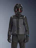 Casaco Alpinestars Cusco Drystar®, preto e cinzento escuro, casaco de motociclismo adventure touring usado com calças técnicas pretas a condizer e um capacete dual-sport, apresentando um design bicolor com painéis em ripstop e logótipos Alpinestars