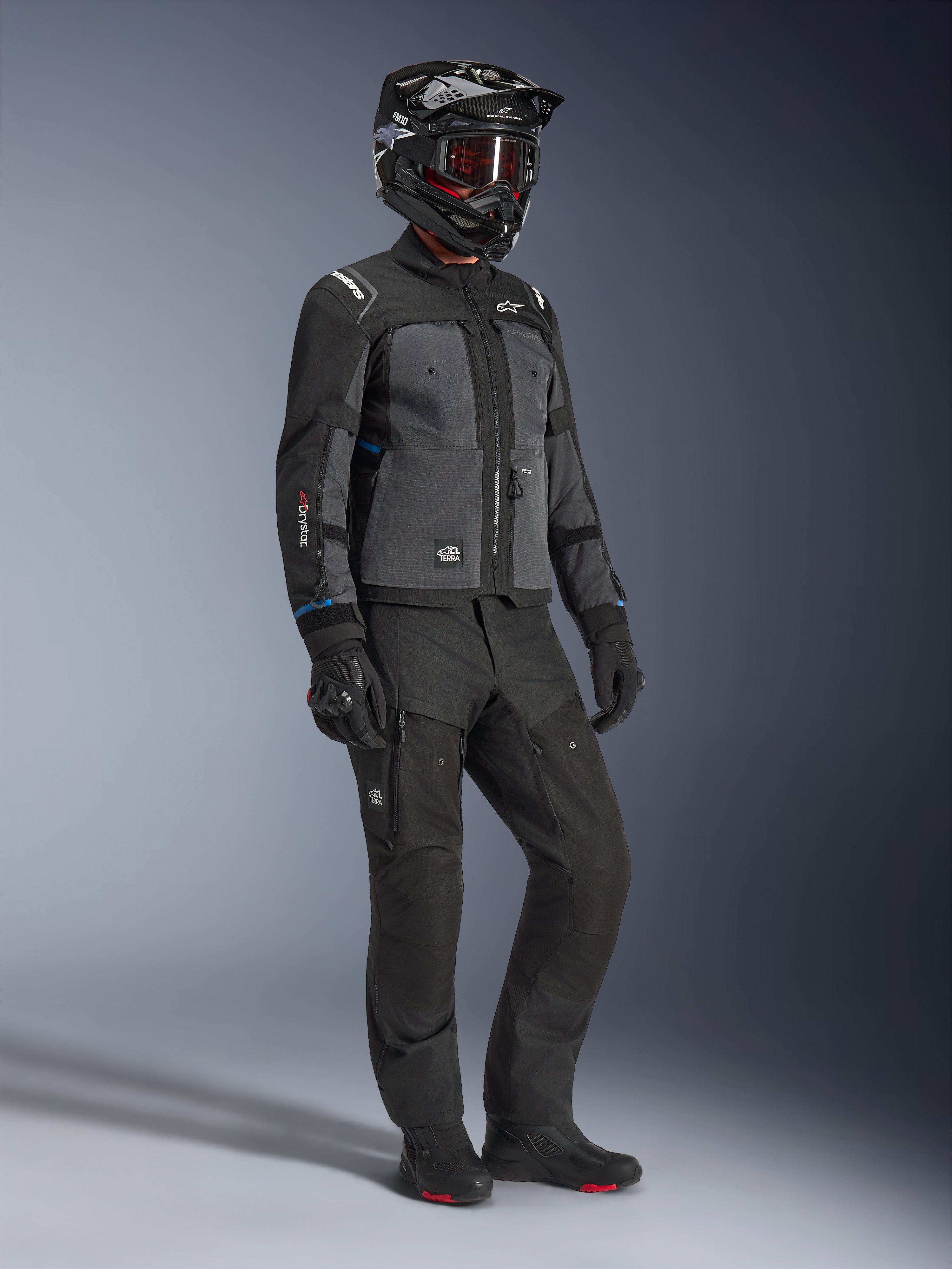 Modelo a usar o Casaco Alpinestars Cusco Drystar® em Preto e Cinzento Escuro, combinado com equipamento completo de motociclismo, incluindo capacete preto, calças técnicas a condizer, luvas e botas, com construção em ripstop e softshell para estrada e turismo de aventura