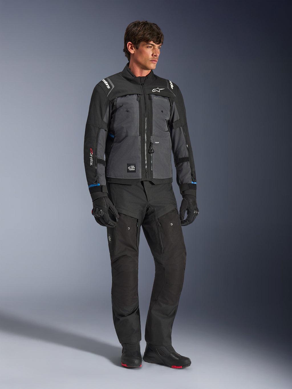 Casaco Alpinestars Cusco Drystar® em Preto e Cinzento Escuro, casaco técnico de motociclismo com painéis multi-tonais, usado com calças e luvas pretas a condizer, concebido para estrada e turismo de aventura.