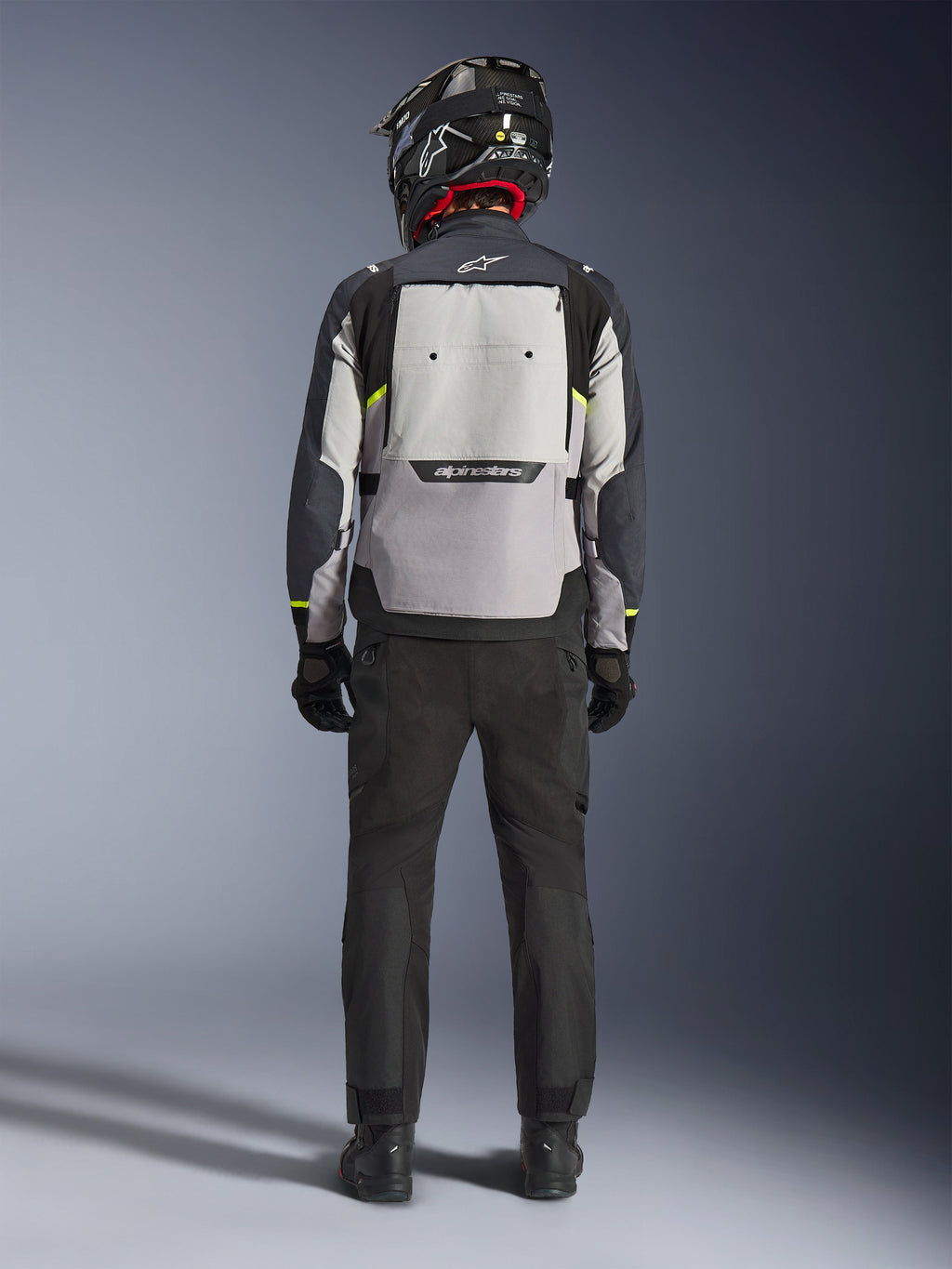 Motociclista visto de costas a usar o Casaco Alpinestars Cusco Drystar® em Ice Gray, Mid Gray e Deep Gray, com um grande painel de ventilação traseiro e logótipo Alpinestars, combinado com calças de condução pretas e capacete preto, vestuário de motociclismo adventure touring