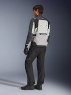 Casaco Alpinestars Cusco Drystar® em Ice Gray, Mid Gray e Deep Gray, vista traseira no modelo, casaco de adventure touring com pormenores em amarelo néon, usado com calças e botas de motociclista pretas, com um grande painel de ventilação nas costas e marca Alpinestars.