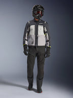 Alpinestars Cusco Drystar® Jacket, cinzento gelo, cinzento médio e cinzento escuro, casaco de motociclismo de aventura usado com calças de condução pretas, luvas pretas e capacete preto com óculos, com painéis cinzentos em blocos de cor e detalhes técnicos para estrada e adventure touring.