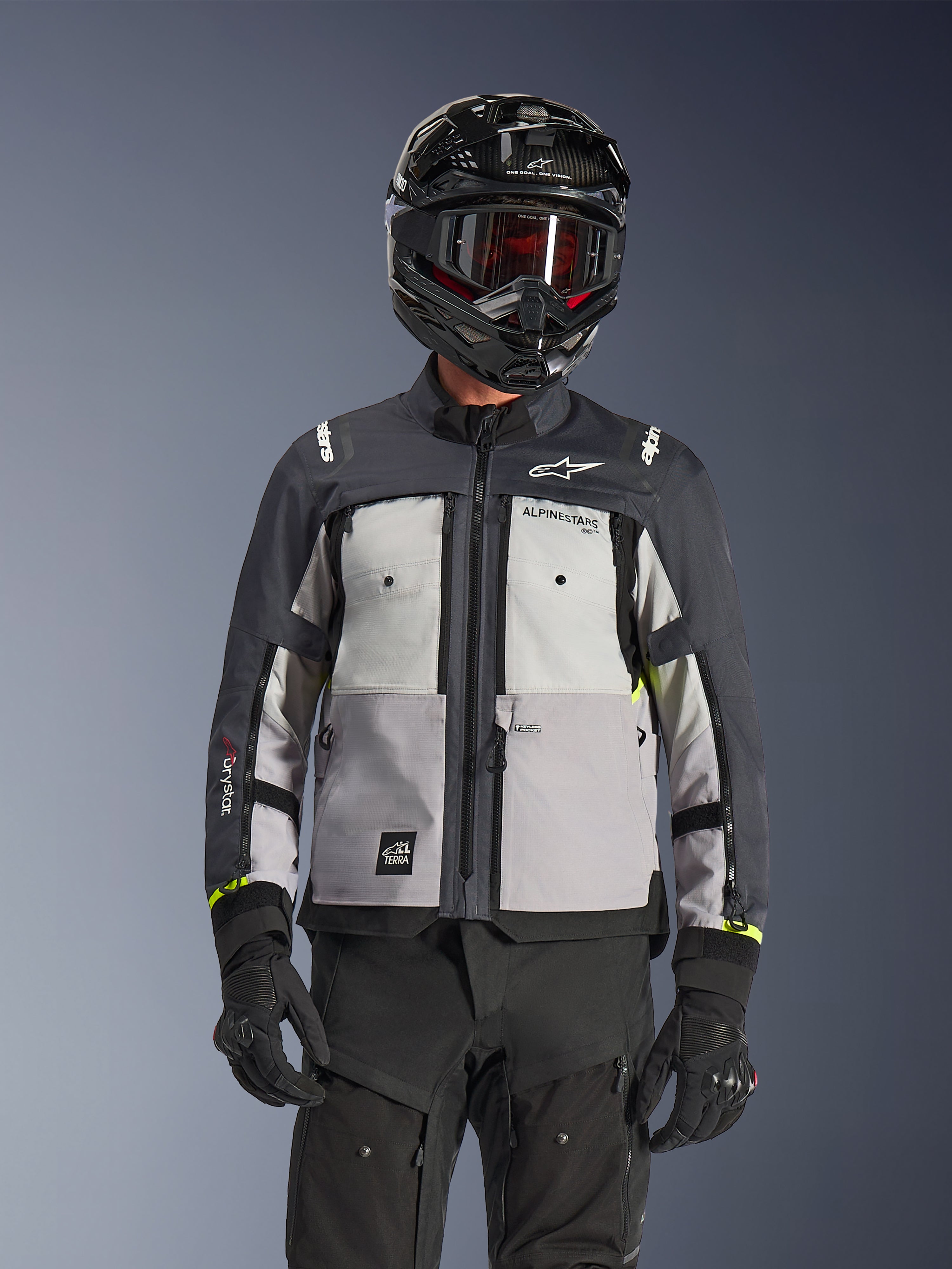 Casaco Alpinestars Cusco Drystar®, casaco adventure touring, Ice Gray, Mid Gray e Deep Gray, com painéis cinzentos em vários tons, aberturas de ventilação no peito com fecho e logótipo Alpinestars, usado por um motociclista com capacete preto e óculos de proteção