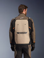 Casaco Alpinestars Cusco Drystar®, Walnut Aluminum Black, vista traseira, com um grande painel traseiro bege e logótipo preto, detalhes laranja, usado com calças e luvas a condizer, concebido para adventure touring