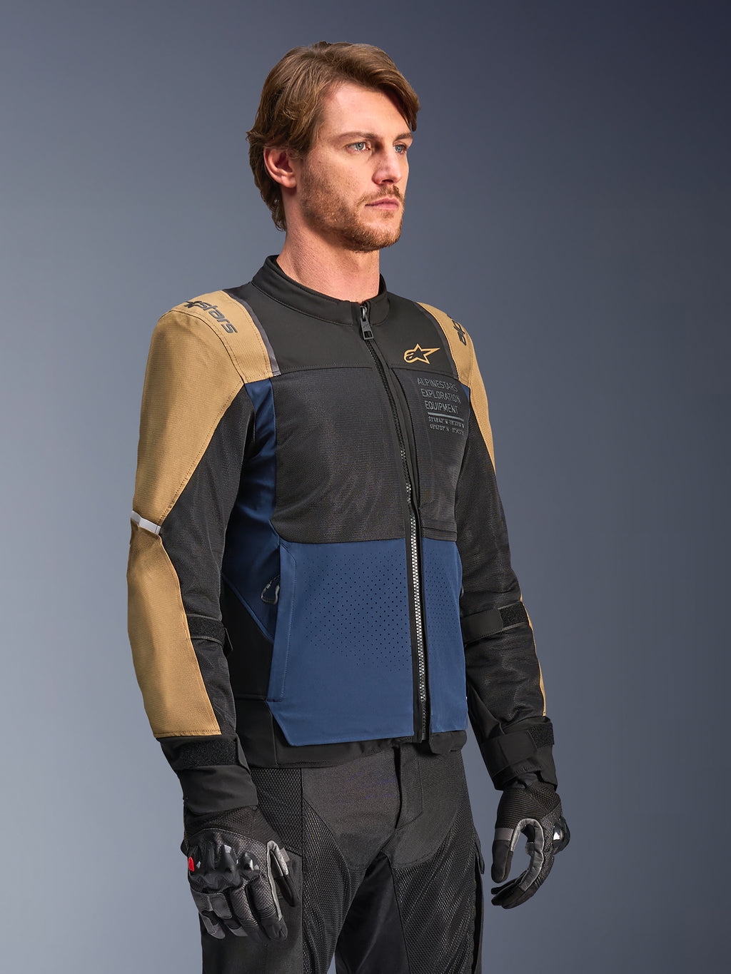 Alpinestars ST-2 Air Jacket, Motorcycle Riding Jacket, Deep Blue, Dark Khaki and Black, featuring high-flow mesh ventilation panels and 'Alpinestars Exploration Equipment' branding, worn with black riding gloves, modern adventure touring design