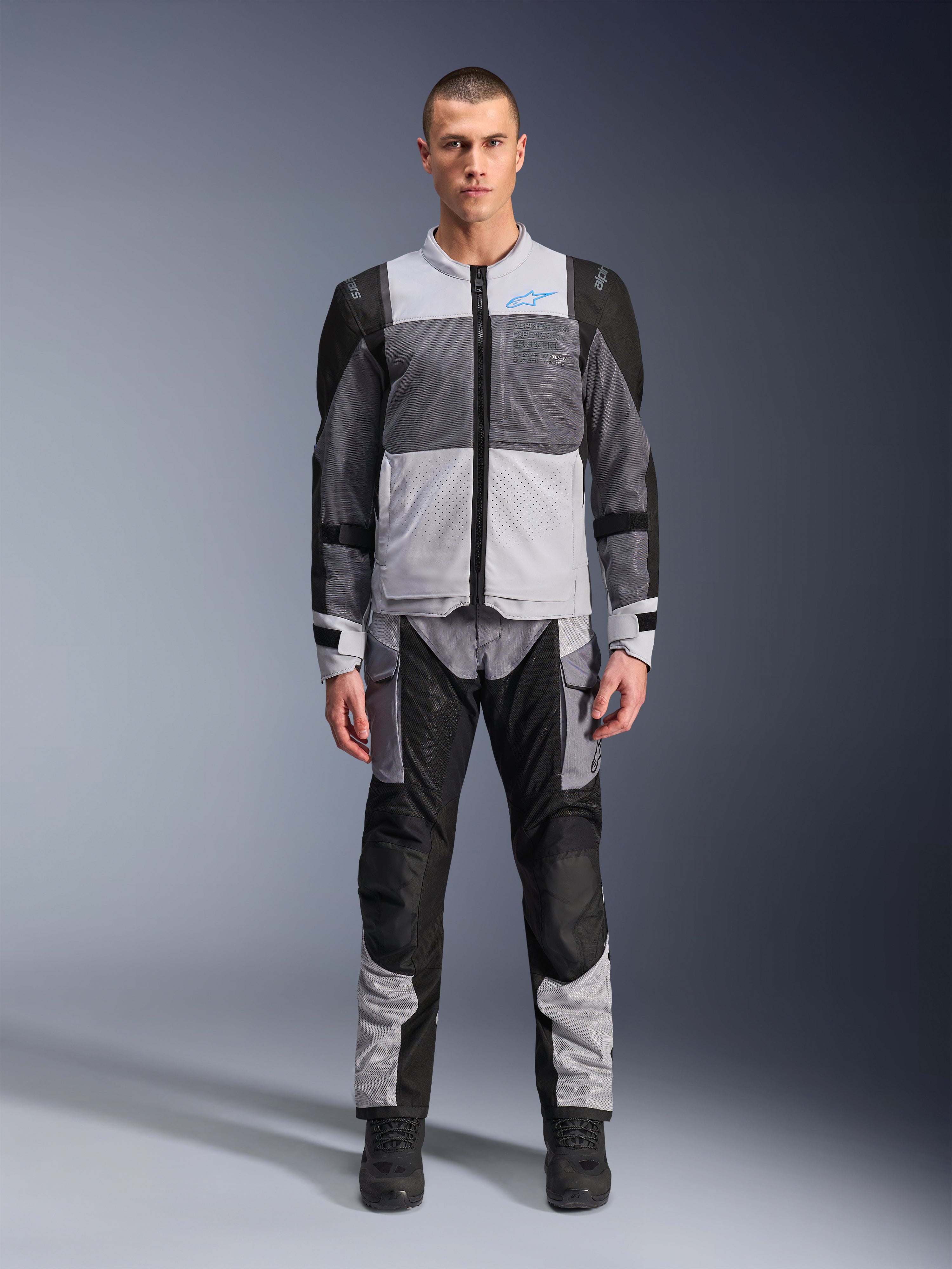 Alpinestars ST-2 Air Jacket, Motorcycle Touring Jacket, Ice Gray Dark Gray and Black, worn by a model with matching adventure pants, featuring large mesh panels, blue Alpinestars logo on chest, and Alpinestars Exploration Equipment branding.