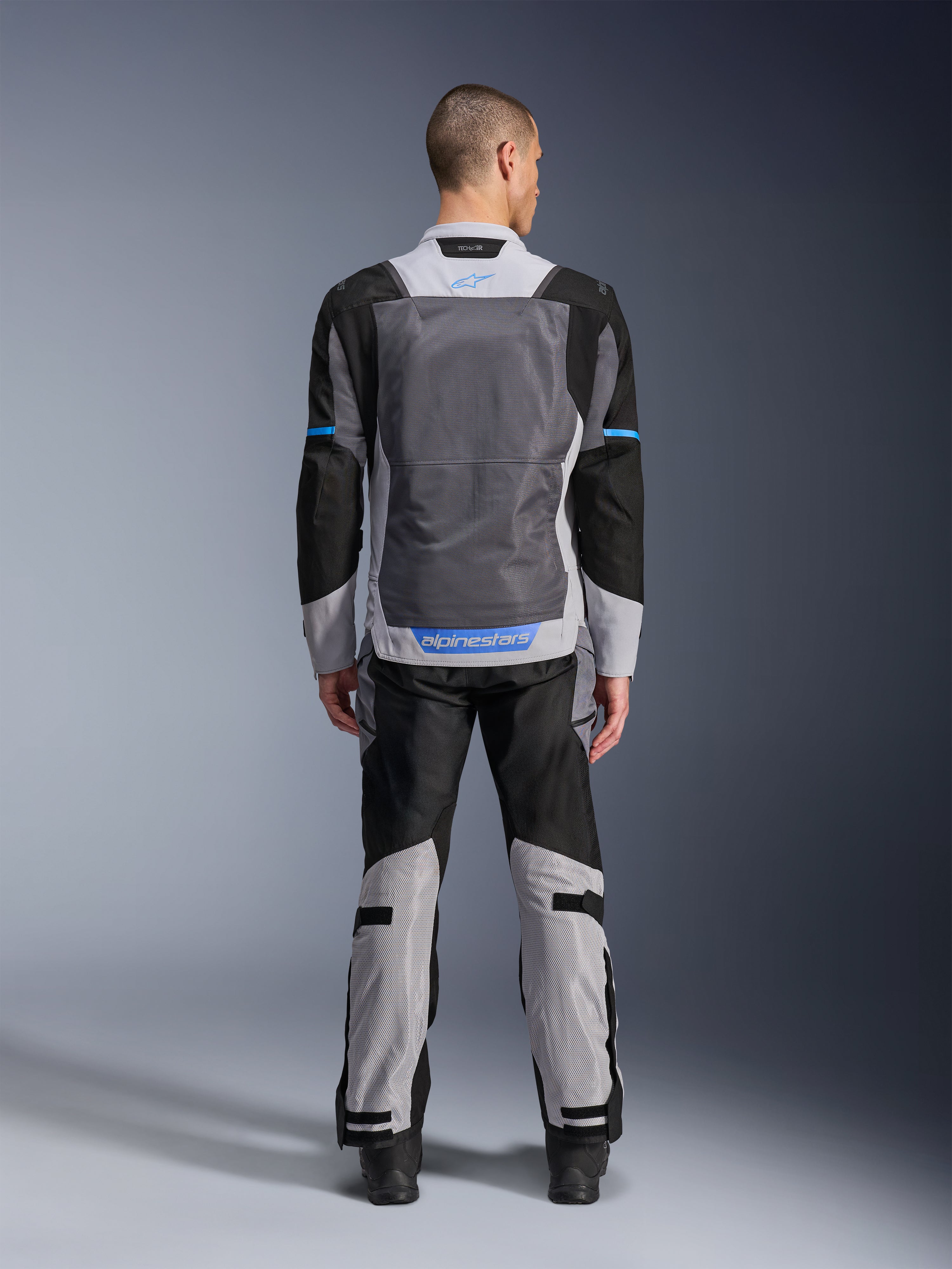 Alpinestars ST-2 Air Jacket, Ice Gray Dark Gray Black, rear view on model, featuring large mesh ventilation panels, blue accents and Alpinestars logo, paired with matching motorcycle pants for adventure touring.