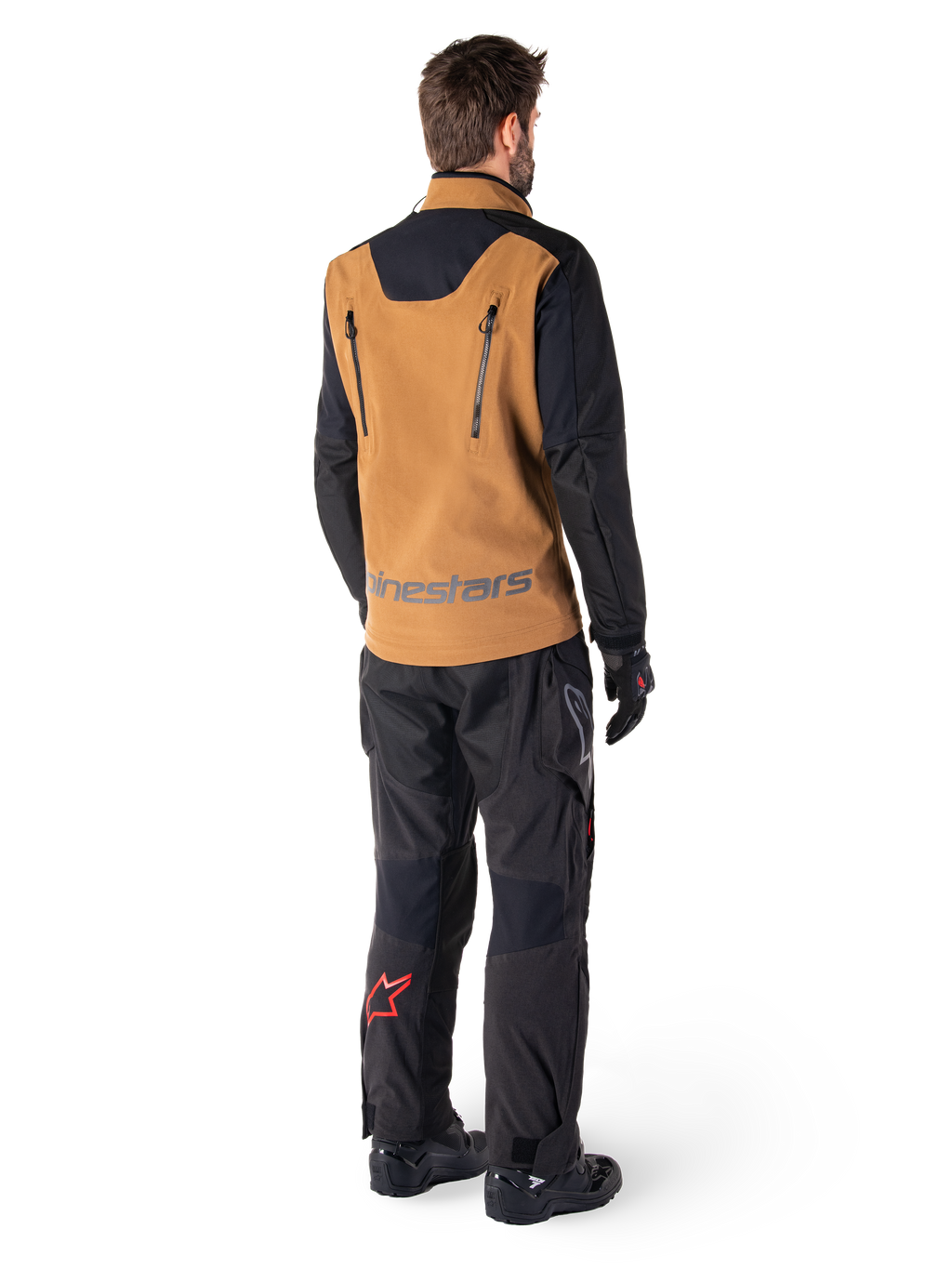 Casaco Alpinestars Hyde XT Stretch Drystar®XF e Calças Hyde XT Drystar®, vista traseira de um piloto com equipamento de adventure touring bege e preto, casaco com fechos verticais nas costas e marca Alpinestars, calças pretas com logótipo de estrela vermelha na barriga da perna, combinado com luvas e botas pretas.