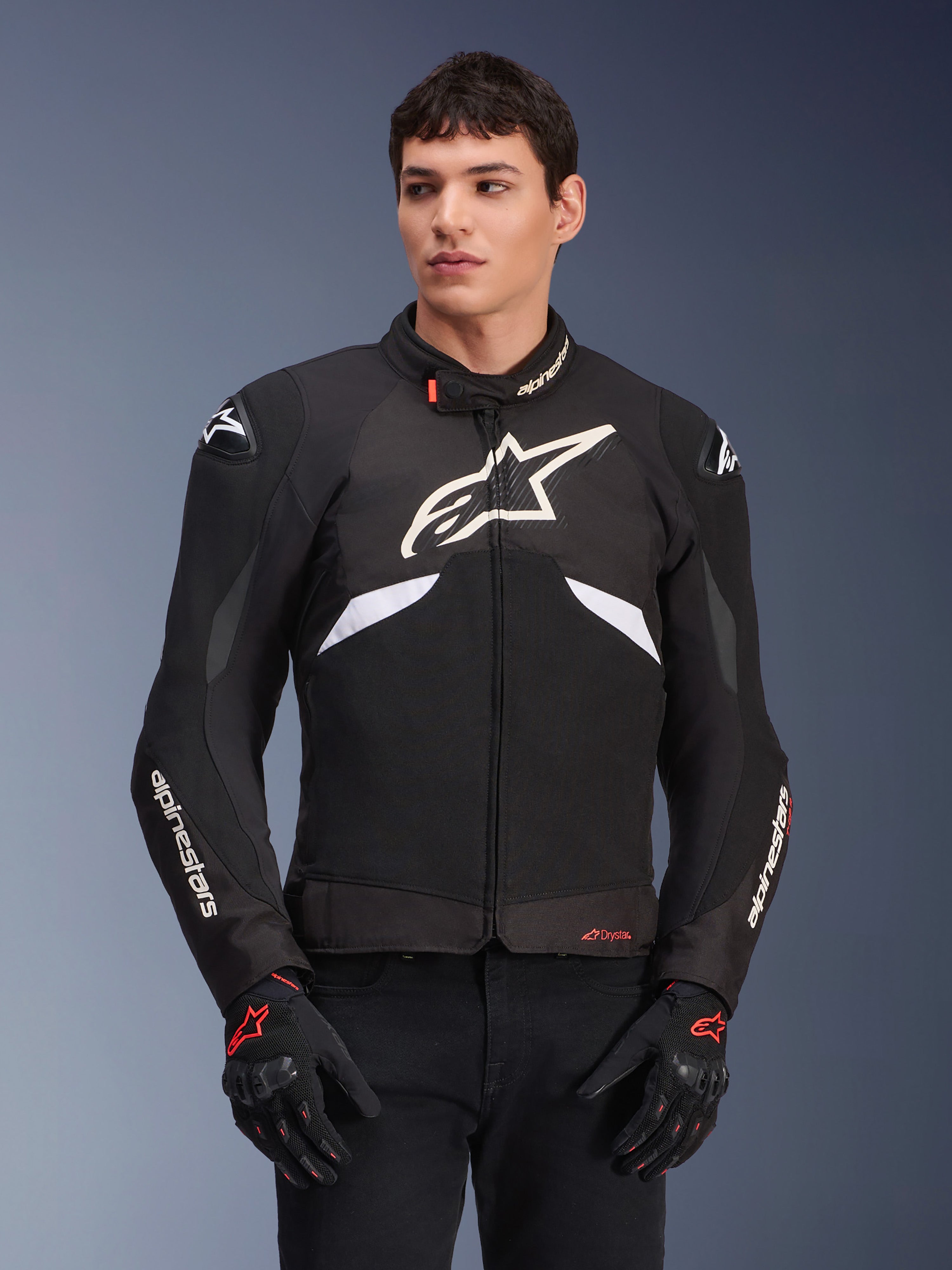 Casaco Alpinestars T-GP R V3 Drystar, casaco têxtil desportivo impermeável, preto e branco com detalhes em vermelho, com um grande logótipo de estrela branco no peito e marca branca nas mangas, usado com luvas de motociclismo pretas e vermelhas
