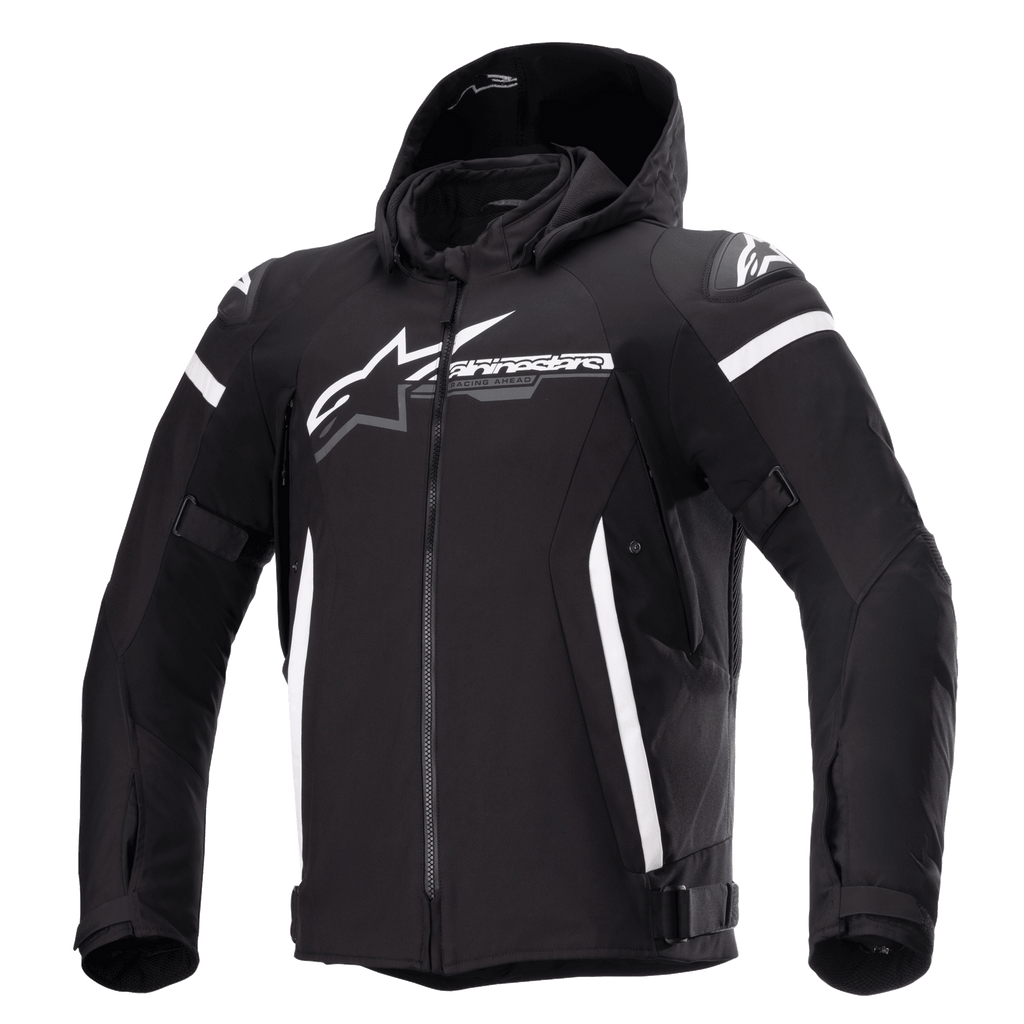 Casaco Alpinestars Zaca Waterproof, casaco de motociclismo preto com capuz removível, logótipo Alpinestars grande em branco no peito, riscas brancas na parte superior dos braços e detalhes laterais verticais, fecho de correr frontal, proteção reforçada nos ombros, correias ajustáveis na cintura e nos braços, construção em tecido softshell