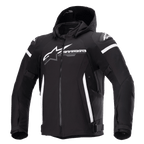 Casaco Alpinestars Zaca Waterproof, casaco de motociclismo preto com capuz removível, logótipo Alpinestars grande em branco no peito, riscas brancas na parte superior dos braços e detalhes laterais verticais, fecho de correr frontal, proteção reforçada nos ombros, correias ajustáveis na cintura e nos braços, construção em tecido softshell