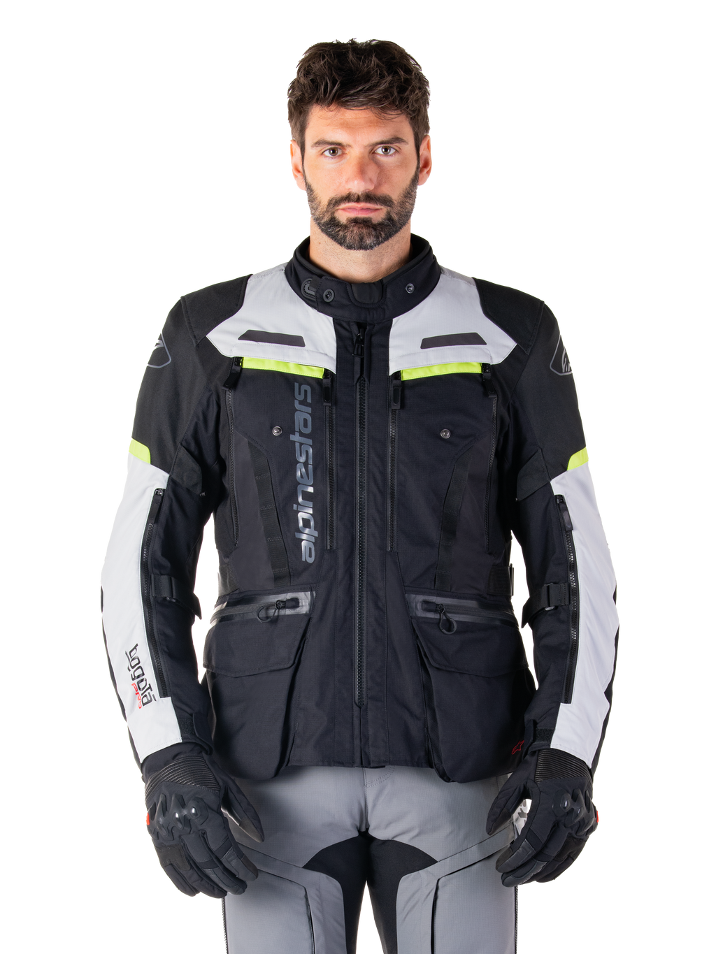 Homem a usar o casaco Alpinestars Bogotá Pro Drystar®, preto, cinzento e amarelo néon, casaco de motociclismo adventure touring para todas as estações, design impermeável com múltiplos bolsos e marca vertical, combinado com luvas pretas e calças de condução cinzentas