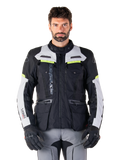 Homem a usar o casaco Alpinestars Bogotá Pro Drystar®, preto, cinzento e amarelo néon, casaco de motociclismo adventure touring para todas as estações, design impermeável com múltiplos bolsos e marca vertical, combinado com luvas pretas e calças de condução cinzentas