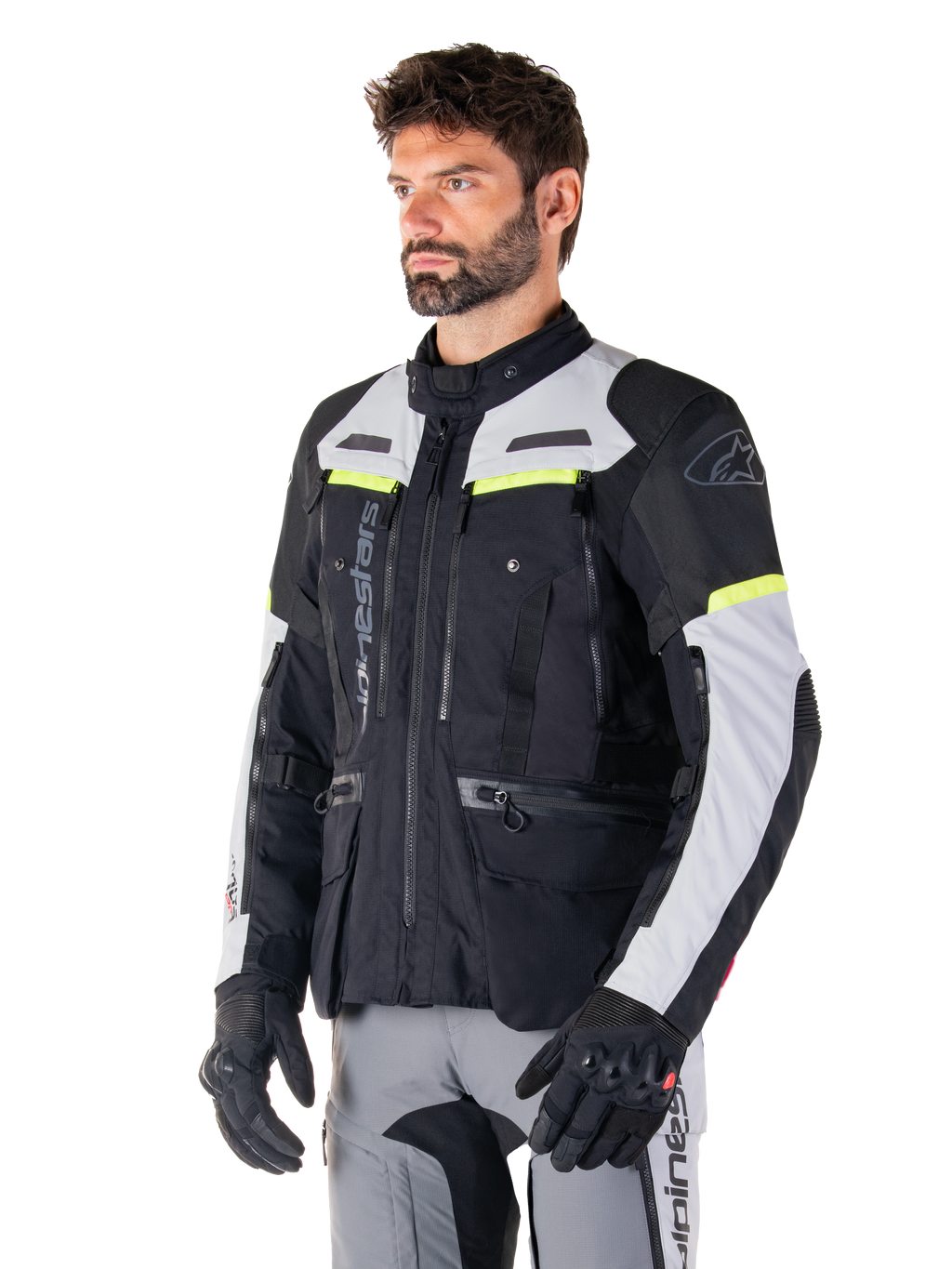 Casaco Alpinestars Bogotá Pro Drystar®, casaco de motociclismo adventure touring, preto, cinzento gelo e amarelo fluo, usado por um homem com calças cinzentas a condizer e luvas pretas, com painéis de ventilação técnicos e design com vários bolsos.