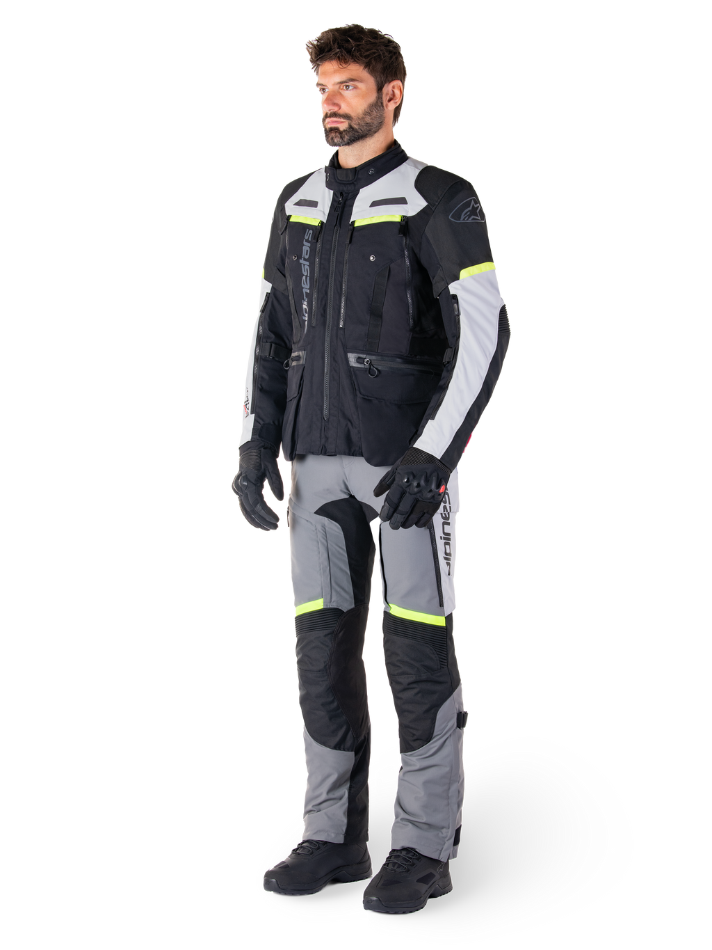 Casaco Alpinestars Bogotá Pro Drystar®, casaco de motociclismo adventure touring, Black Ice Gray Yellow Fluo, usado por um modelo com calças a condizer e luvas pretas, com construção têxtil impermeável, painéis de ventilação e pormenores fluorescentes.