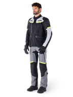 Casaco Alpinestars Bogotá Pro Drystar®, casaco de motociclismo adventure touring, Black Ice Gray Yellow Fluo, usado por um modelo com calças a condizer e luvas pretas, com construção têxtil impermeável, painéis de ventilação e pormenores fluorescentes.