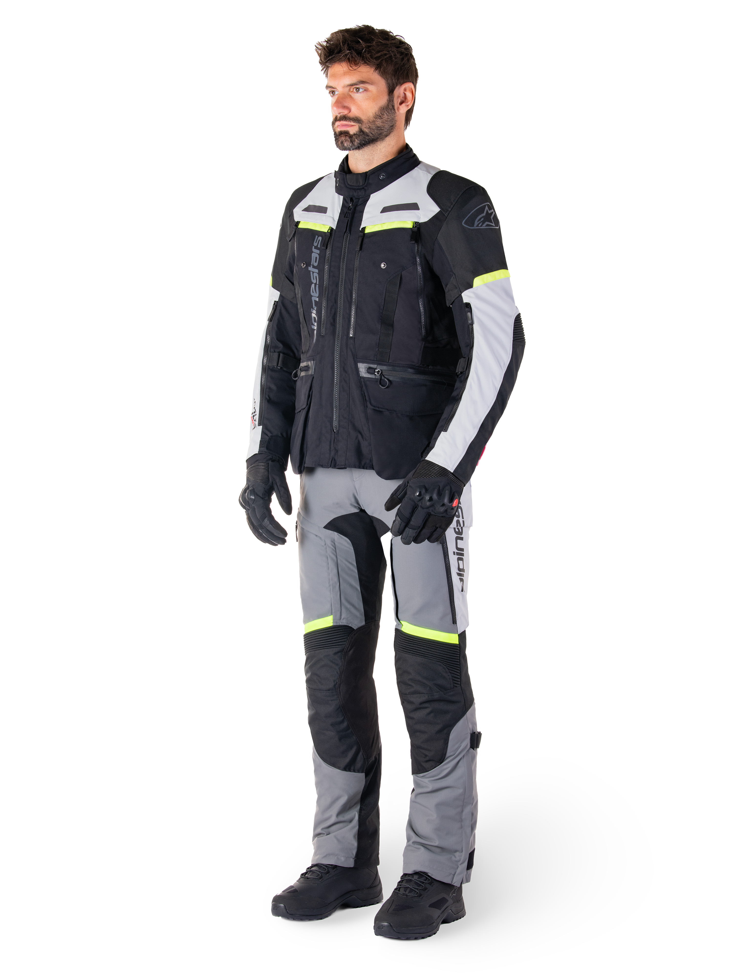 Casaco Alpinestars Bogotá Pro Drystar®, casaco de motociclismo adventure touring, Black Ice Gray Yellow Fluo, usado por um modelo com calças a condizer e luvas pretas, com construção têxtil impermeável, painéis de ventilação e pormenores fluorescentes.