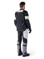 Vista traseira de um motociclista a vestir o Casaco Alpinestars Bogotá Pro Drystar® em Preto Ice Gray Amarelo Fluo, combinado com calças de adventure touring a condizer, com um bolso traseiro grande e detalhes em amarelo fluorescente, equipamento de motociclismo têxtil para todas as estações.