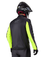 Casaco Alpinestars Bogotá Pro Drystar®, vista traseira, preto com mangas amarelo fluo, usado por um motociclista com capacete e luvas pretas, equipamento de motociclismo adventure touring de alta visibilidade com acabamento têxtil técnico.