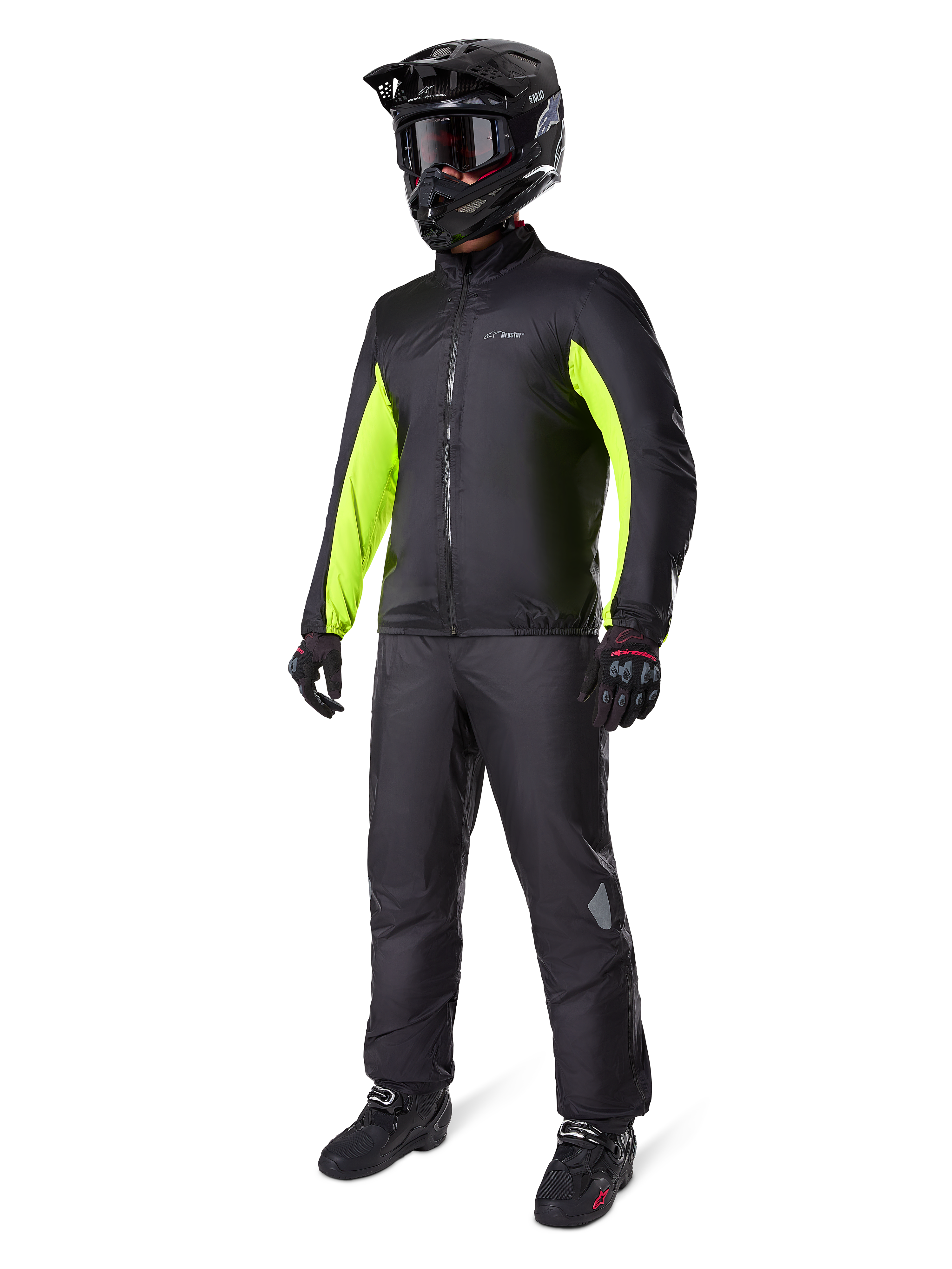 Motociclista a usar o forro do casaco Alpinestars Bogotá Pro Drystar®, preto com painéis em amarelo néon brilhante nas mangas, usado com calças pretas a condizer, capacete de motocross preto e luvas, equipamento de aventura impermeável para todas as estações