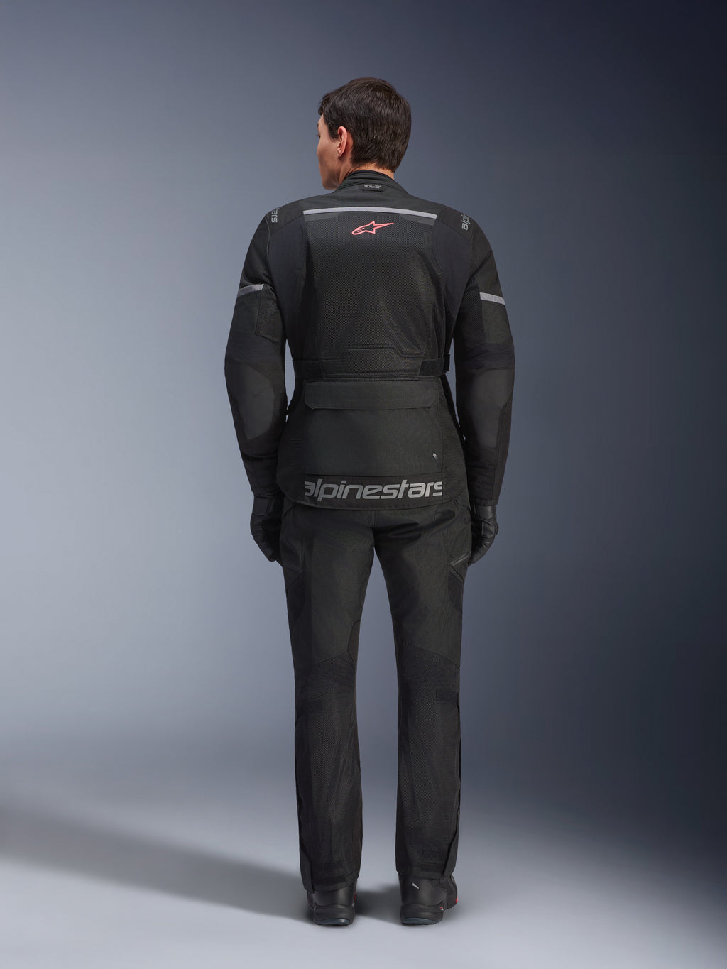 Casaco e Calças Alpinestars Andes Air Drystar®, equipamento de touring para motociclismo em preto, vista traseira do piloto, com painéis em malha, logótipo de estrela vermelha e marca Alpinestars refletora no casaco, usado com luvas e botas pretas