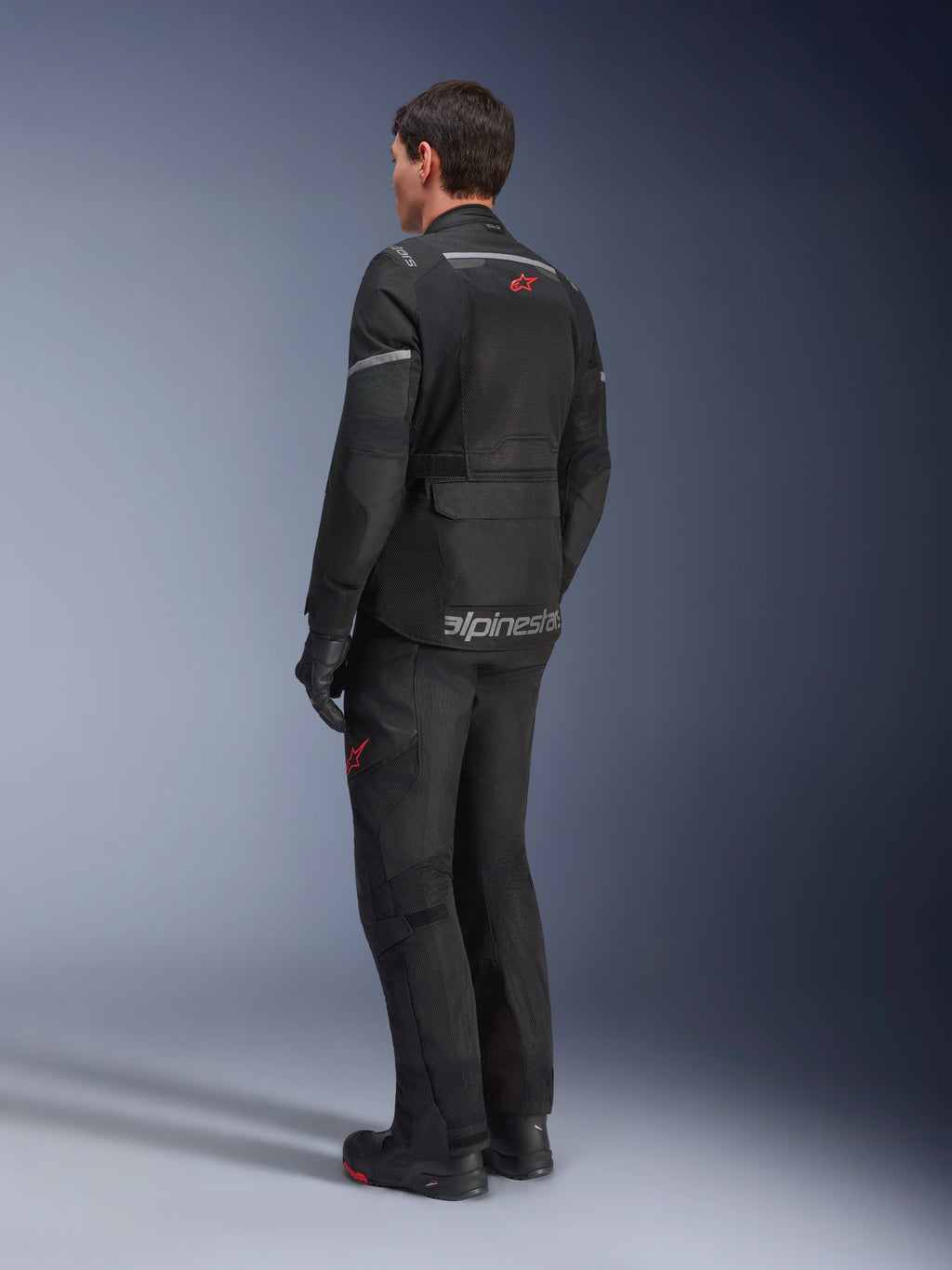 Casaco Alpinestars Andes Air Drystar®, preto, vista traseira num motociclista, com painéis de malha extensos para ventilação, usado com calças e botas de motociclismo de aventura a condizer, demonstrando o design de touring e a imagem da marca.
