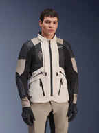 Alpinestars AMT-10LAB Drystar® XF Jacket, White Sand Aluminum Camo, casaco de aventura para motociclismo com painéis de malha MATRYX® pretos e reforços em couro, usado por um modelo com luvas pretas e calças cor de areia a condizer, retrato de estúdio