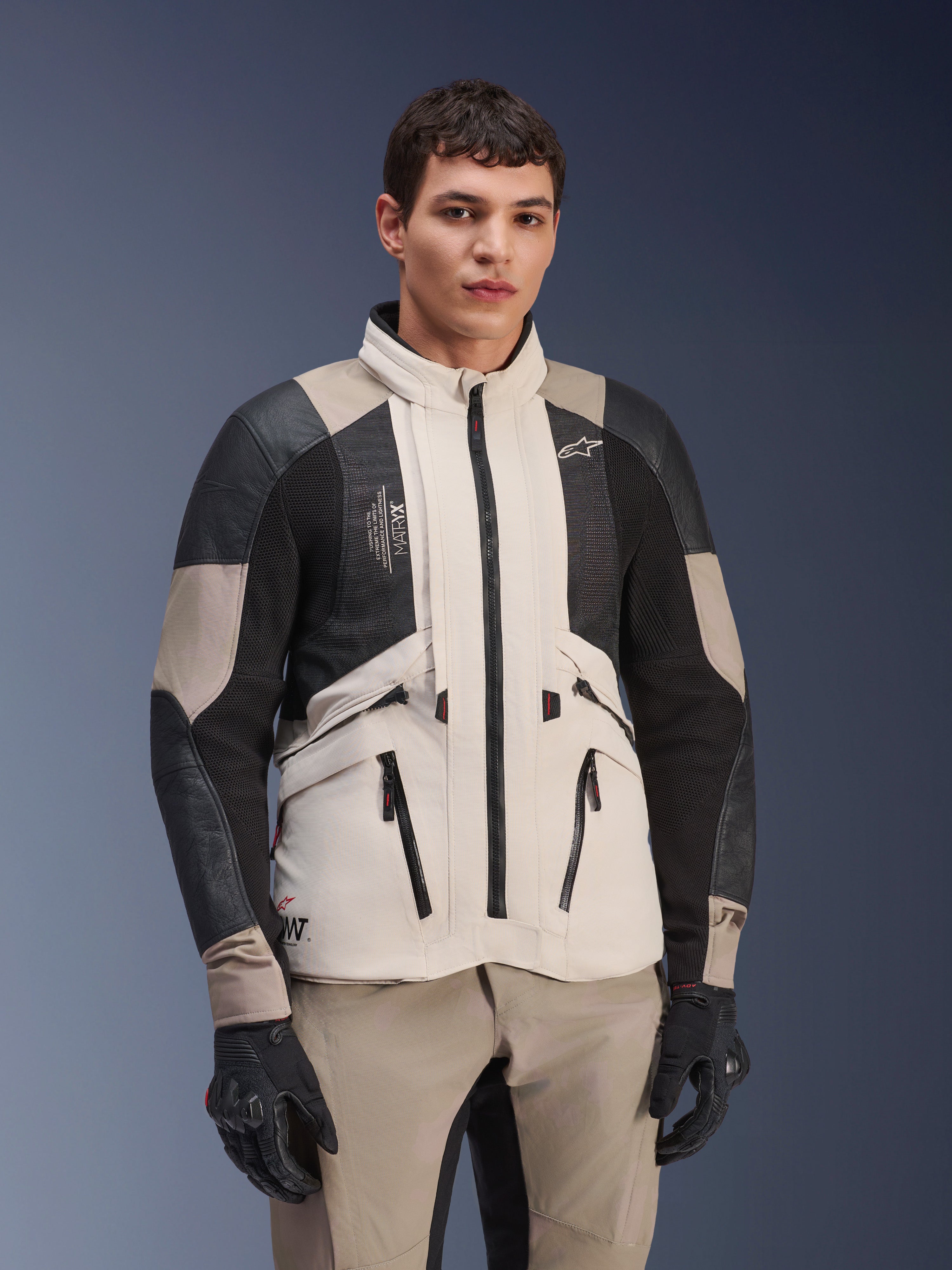 Alpinestars AMT-10LAB Drystar® XF Jacket, White Sand Aluminum Camo, casaco de aventura para motociclismo com painéis de malha MATRYX® pretos e reforços em couro, usado por um modelo com luvas pretas e calças cor de areia a condizer, retrato de estúdio