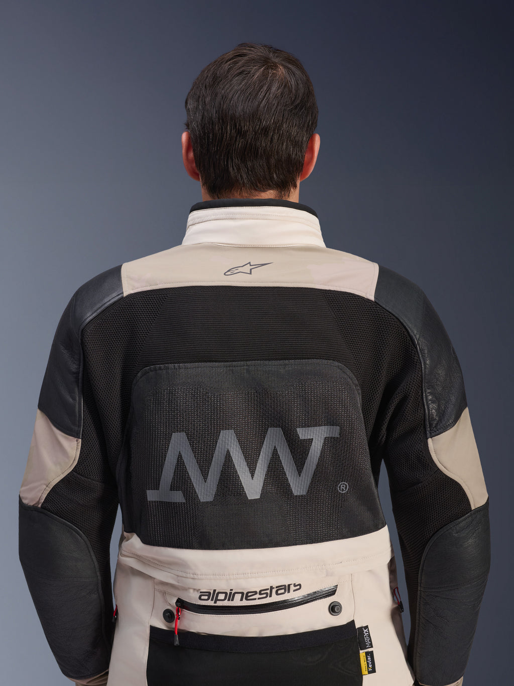 Vista traseira do Casaco Alpinestars AMT-10LAB Drystar® XF em White Sand e preto, com um logótipo AMT grande no painel traseiro em malha, marca Alpinestars na zona inferior das costas e construção em têxtil técnico para motociclismo de aventura.