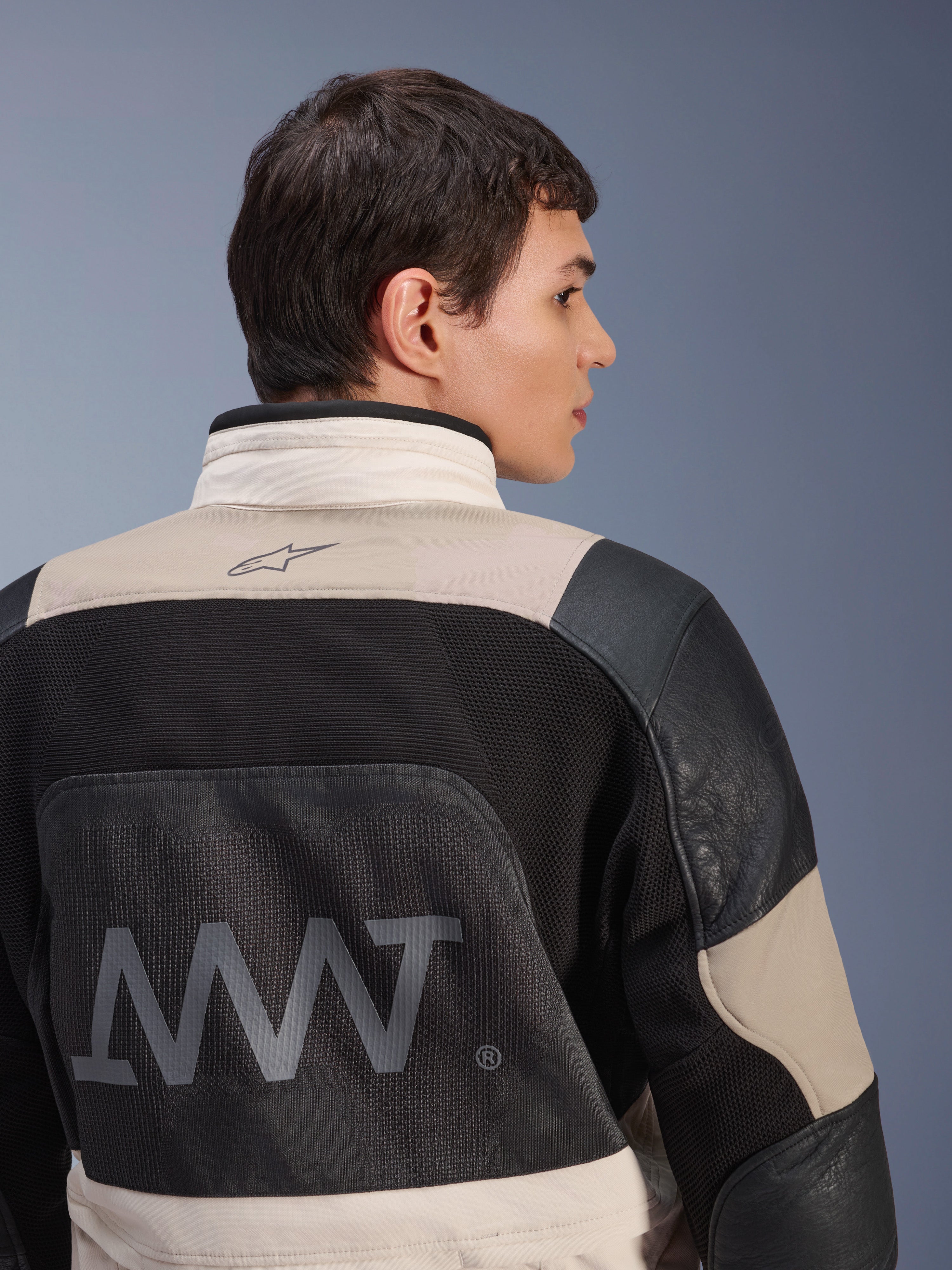 Casaco Alpinestars AMT-10LAB Drystar® XF, vista traseira num modelo masculino, cores White Sand Aluminum Camo e preto, com logótipo AMT de grandes dimensões, painéis de ventilação em malha e reforços em couro, vestuário técnico de motociclismo de aventura