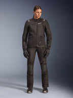 Motociclista feminina com o casaco Alpinestars Stella Andes V4 Drystar® em preto, combinado com calças e luvas de adventure-touring pretas a condizer, construção em têxtil técnico com múltiplos bolsos utilitários, logótipo Alpinestars em branco, equipamento de motociclismo completo para todas as condições climatéricas
