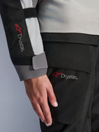 Detalhe em grande plano da manga do casaco Stella Andes V4 Drystar® para mulher e calças a condizer da Alpinestars, com o logótipo Drystar, construção têxtil em cinzento gelo e preto, marcação de impermeabilidade para equipamento de aventura touring