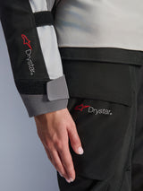 Close-up detail of the Alpinestars Woman Stella Andes V4 Drystar® Jacket sleeve and matching pants, featuring the Drystar logo, ice gray and black textile construction, waterproof branding for adventure touring gear