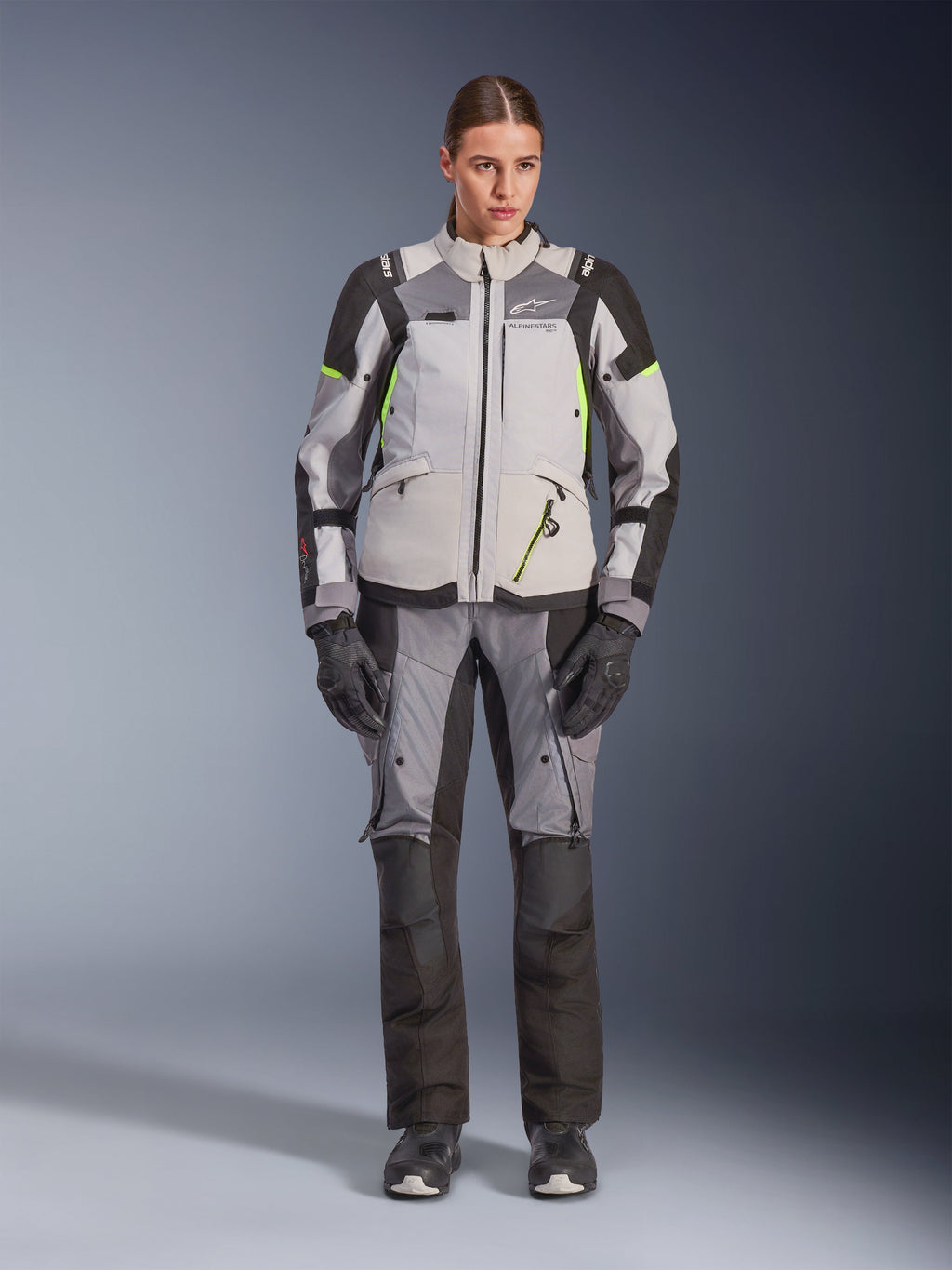 Casaco Alpinestars Stella Andes V4 Drystar® para Mulher, cinza gelo e cinza escuro com pormenores em preto e amarelo fluo, usado com calças e luvas de motociclismo a condizer, equipamento de adventure-touring impermeável para mulher
