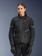 Alpinestars Stella Andes Air Drystar Jacket, casaco de motociclismo de turismo para mulher, preto com detalhes cinzentos e um pequeno logótipo vermelho, com painéis de ventilação em malha, gola alta e múltiplos bolsos utilitários, usado com luvas e calças de condução a condizer
