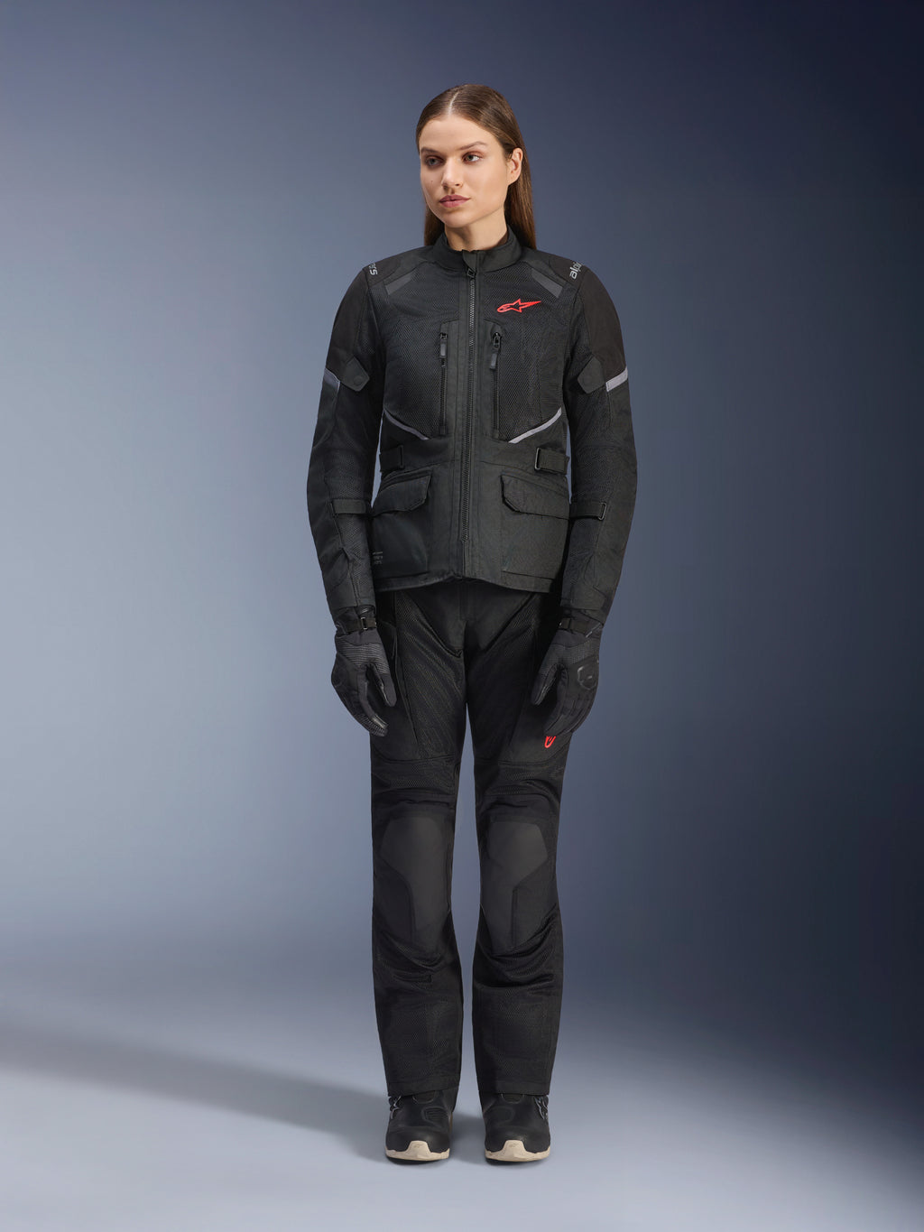 Modelo feminina a usar o casaco Alpinestars Stella Andes Air Drystar® em preto, combinado com calças de turismo e luvas pretas a condizer, com grandes painéis de ventilação em malha, detalhes do logótipo em vermelho e elementos refletores, fotografia profissional de estúdio de equipamento de motociclismo para mulher.