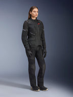 Mulher a usar o Casaco Alpinestars Stella Andes Air Drystar®, casaco têxtil de aventura e touring em preto, combinado com calças e luvas pretas a condizer, com grandes painéis de ventilação em malha e logótipo vermelho, conjunto coordenado de motociclismo para mulher