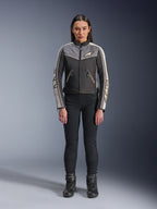 Mulher a usar o casaco Alpinestars Stella T-Dyno WR, preto, cinzento escuro e cru, vista frontal, casaco de motociclismo têxtil com design de inspiração vintage, com logótipo no peito e nas mangas, usado com calças e botas pretas