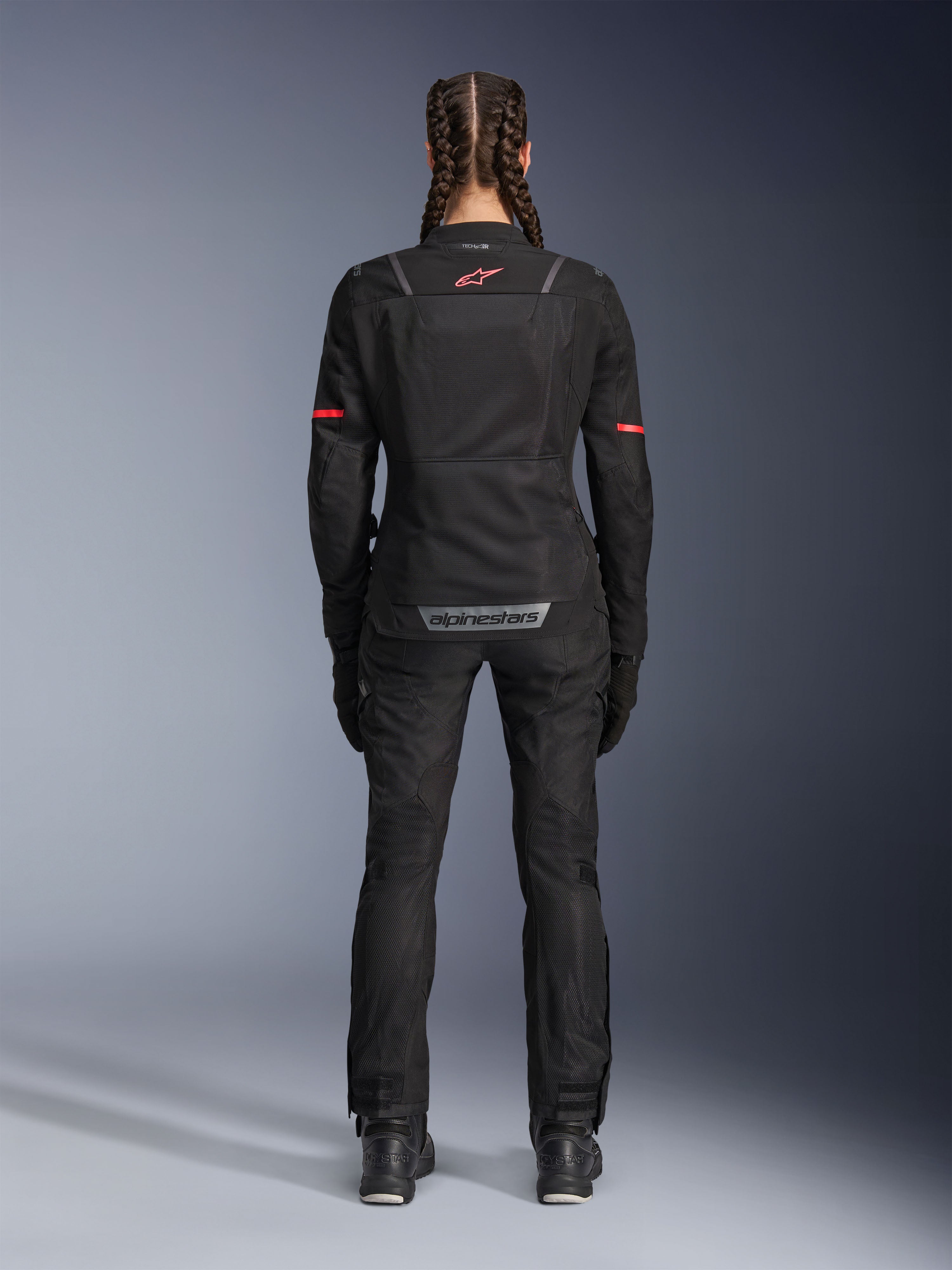 Calças Alpinestars Stella Andes Air Drystar®, calças de motociclismo para mulher, pretas, vista traseira, usadas com um blusão de malha a condizer com detalhes em vermelho, realçando os painéis de ventilação em malha e a marca refletora na parte inferior das costas, concebidas para aventura e touring