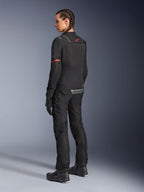 Casaco Alpinestars Stella ST-2 Air, casaco de motociclismo para mulher, preto com detalhes vermelhos nas mangas e na parte superior das costas, vista traseira de modelo a usar calças e botas de motociclismo pretas a condizer, com logótipos Alpinestars refletores e construção têxtil moderna.