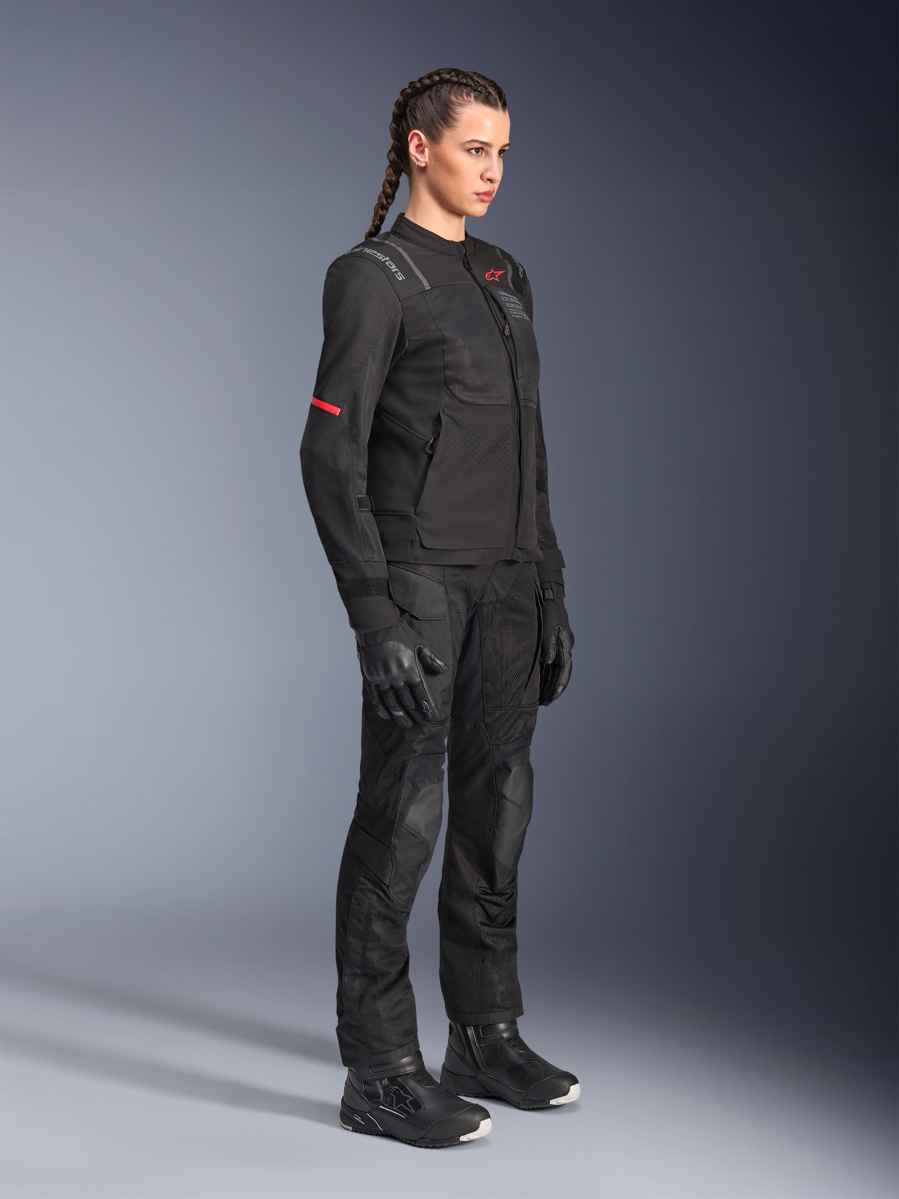 Motociclista feminina a usar calças Alpinestars Stella Andes Air Drystar® em preto, calças de aventura em têxtil com painéis de ventilação em malha, combinadas com casaco Stella, luvas e botas a condizer para um conjunto completo de motociclismo de touring.