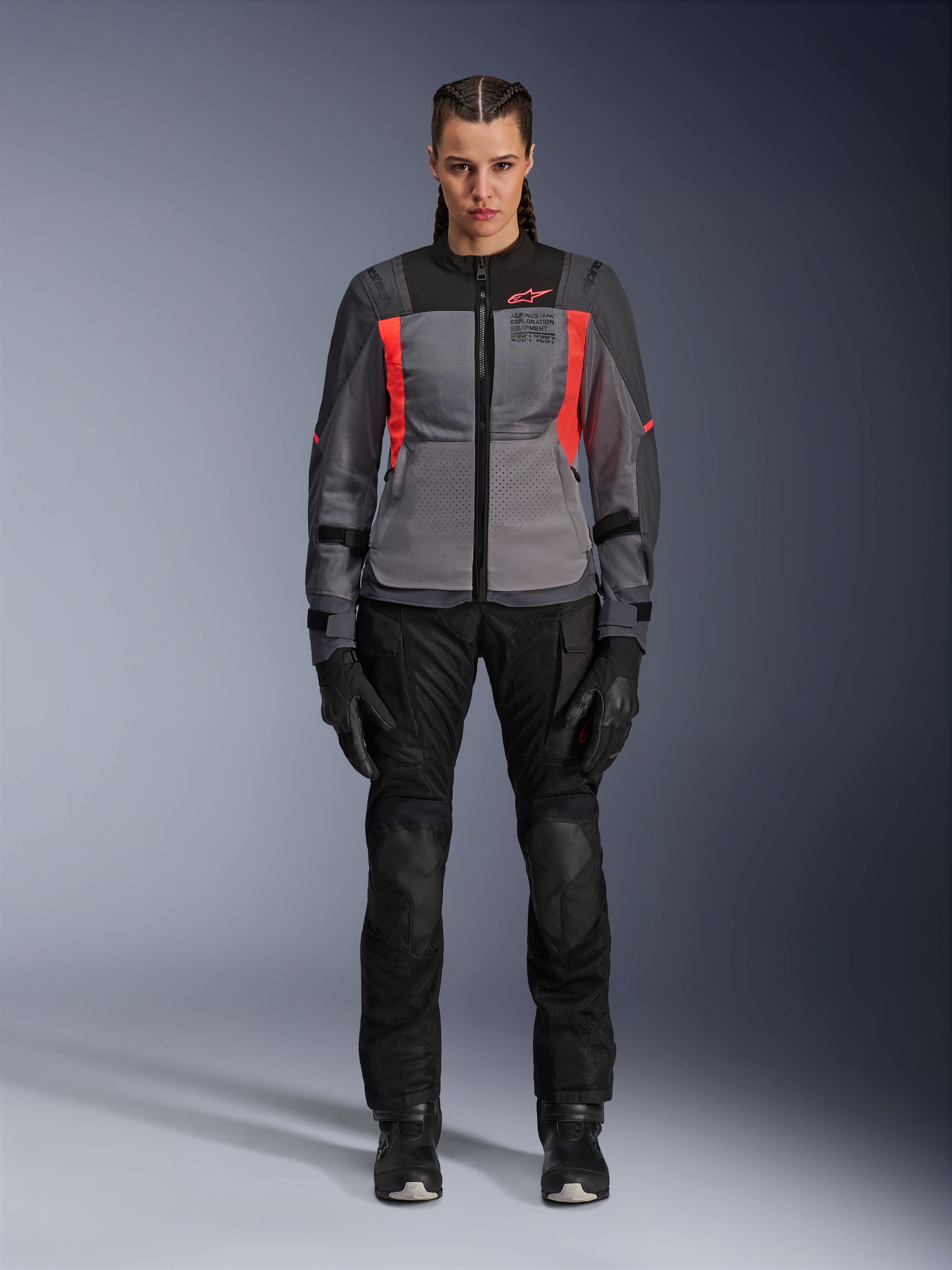 Mulher a usar o Casaco Alpinestars Stella ST-2 Air em cinzento escuro e coral fluorescente, combinado com calças e luvas de motociclismo pretas, vista frontal, equipamento moderno de malha para turismo e aventura para mulher