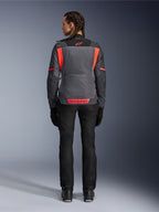 Vista traseira de uma modelo a usar o Casaco Alpinestars Stella St-2 Air em Cinzento Profundo e Cinzento Escuro com detalhes Coral Fluo, apresentando grandes painéis de ventilação em malha nas costas e pormenores de logótipo refletores, combinada com calças e luvas de motociclismo pretas.