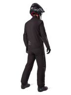 Motorcycle rider seen from behind wearing the black Amt-8 Stretch Drystar® XF Pants and matching jacket, complete adventure touring outfit with black helmet and boots, technical waterproof and stretchable gear for long-range motorcycling