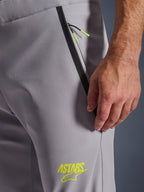 Calças Alpinestars Aeroshell, cinzento médio com detalhes em amarelo néon, vista em pormenor do bolso frontal com fecho de correr, acabamento em fita preta e cordões amarelos vibrantes, logótipo ASTARS amarelo na coxa, material softshell elástico para motociclismo