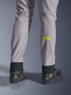 Calças Alpinestars Aeroshell, cinzento médio com logótipo Astars em amarelo fluo na barriga da perna, vistas de trás com calçado de motociclismo preto, apresentando uma bainha inferior elástica e uma silhueta afunilada moderna