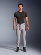 Modelo masculino a usar Calças Alpinestars Aeroshell em Cinzento Médio e Amarelo Fluo, calças softshell desportivas crossover com cintura elástica com cordão e bolsos com fecho de correr, combinadas com uma t-shirt de performance preta de manga curta, design atlético moderno para condução em estrada e casual