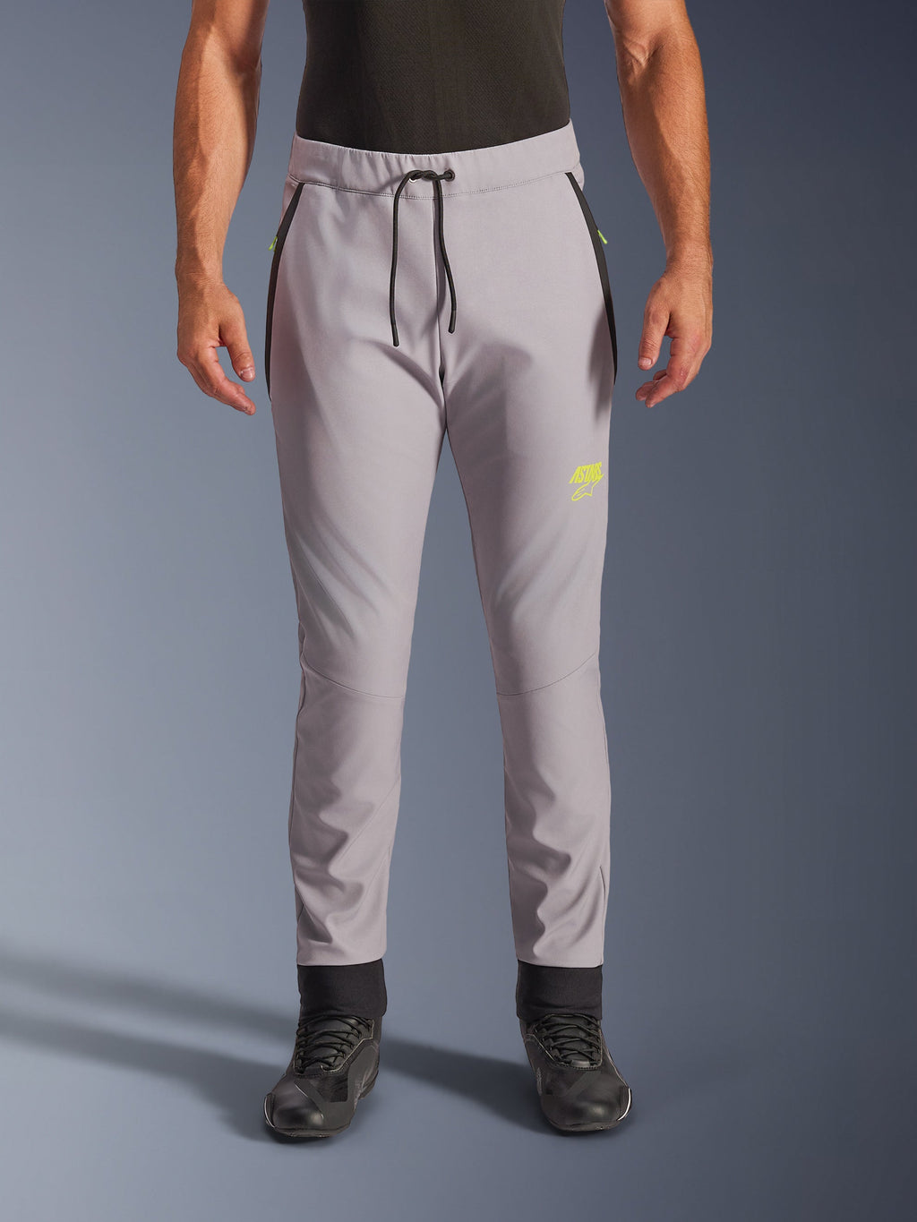 Alpinestars Aeroshell Pants, cinzento médio e amarelo fluo, calças de motociclismo softshell crossover, com cintura de cordão preto e punhos ajustados nos tornozelos, logótipo amarelo na coxa esquerda, joelhos pré-curvados, silhueta desportiva estilo jogger