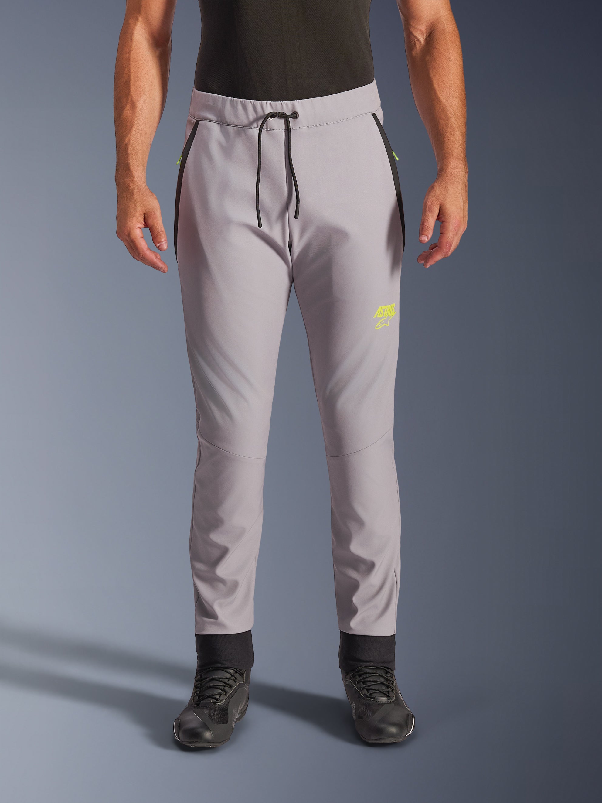 Alpinestars Aeroshell Pants, cinzento médio e amarelo fluo, calças de motociclismo softshell crossover, com cintura de cordão preto e punhos ajustados nos tornozelos, logótipo amarelo na coxa esquerda, joelhos pré-curvados, silhueta desportiva estilo jogger